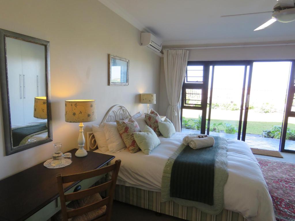 a bedroom with a bed and a desk and windows at The Beach House in Port Alfred