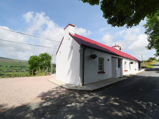 um pequeno edifício branco com um telhado vermelho numa estrada em Kerrigan's Cottage em Commeen