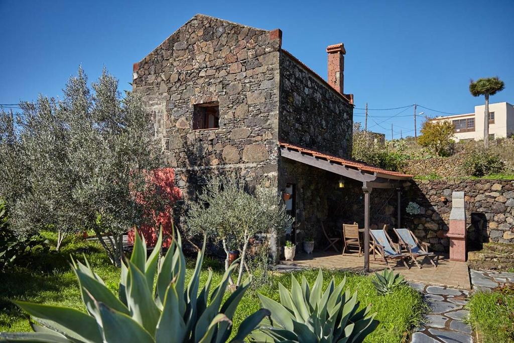 een stenen huis met een patio en stoelen in een tuin bij Casa Rural Sanjora in Valverde