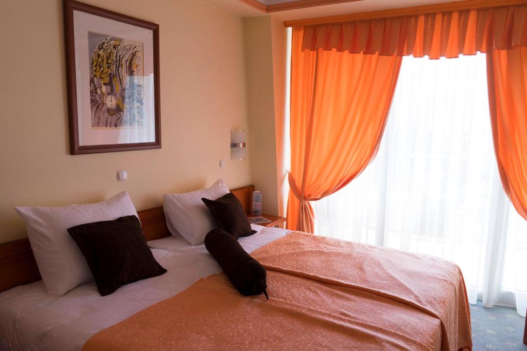 ストルガにあるHotel Drimのベッドルーム1室(オレンジ色のカーテンと窓付きのベッド1台付)