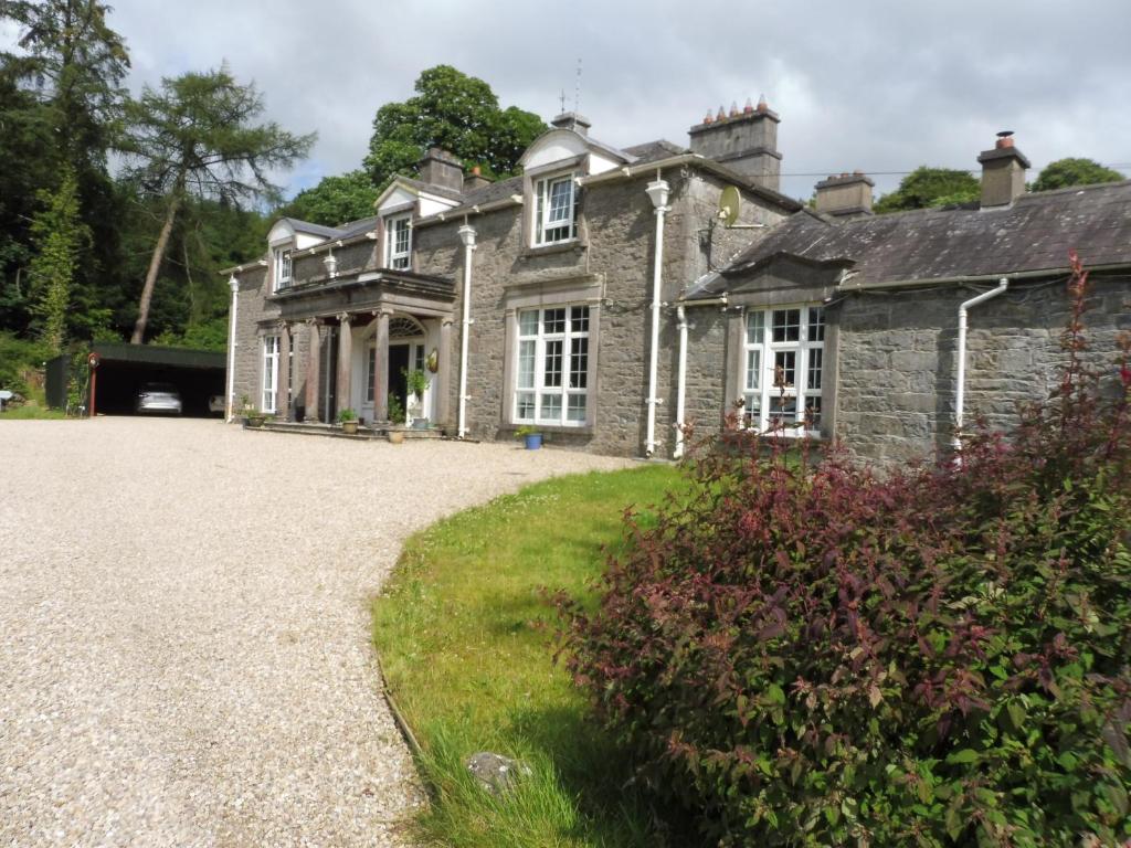 an old stone house with a gravel driveway at Ross House Equestrian Holidays in Mountnugent