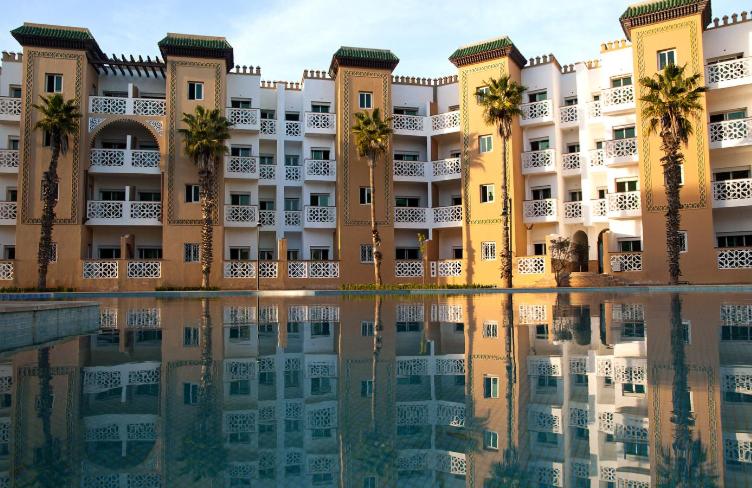 een gebouw met palmbomen en een zwembad met water bij Al Kawtar in Mohammedia