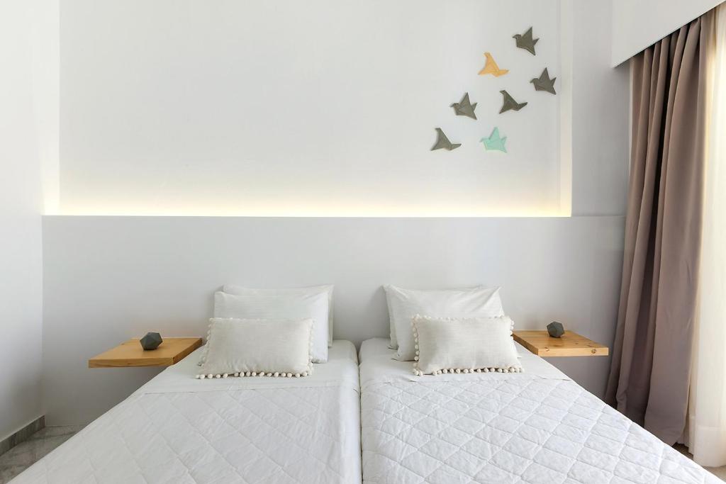 a bedroom with two beds with white sheets and birds on the wall at Memories Beach Hotel in Monolithos