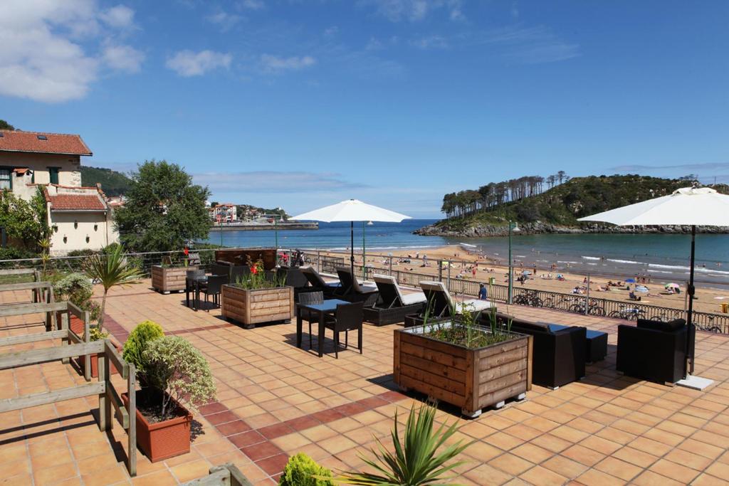 een terras met tafels en parasols en een strand bij Hotel Metrokua in Lekeitio