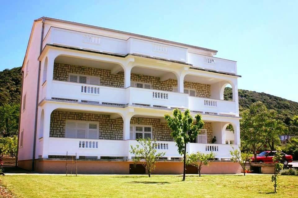 un bâtiment rose avec des arbres devant lui dans l'établissement Rooms Viskic, à Rab