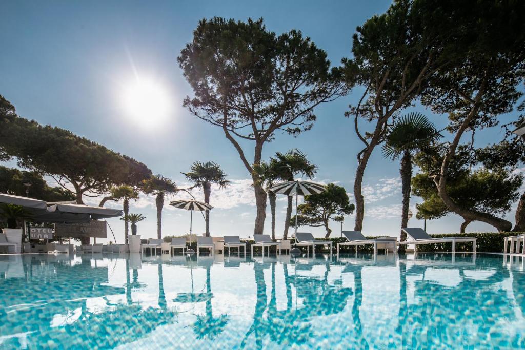 a swimming pool with chairs and umbrellas at Hotel Bellavista in Lignano Sabbiadoro