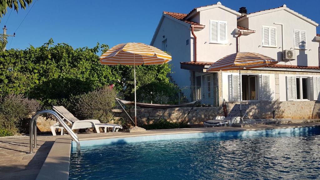 a swimming pool with two umbrellas and a house at Apartman Vojaline in Milna
