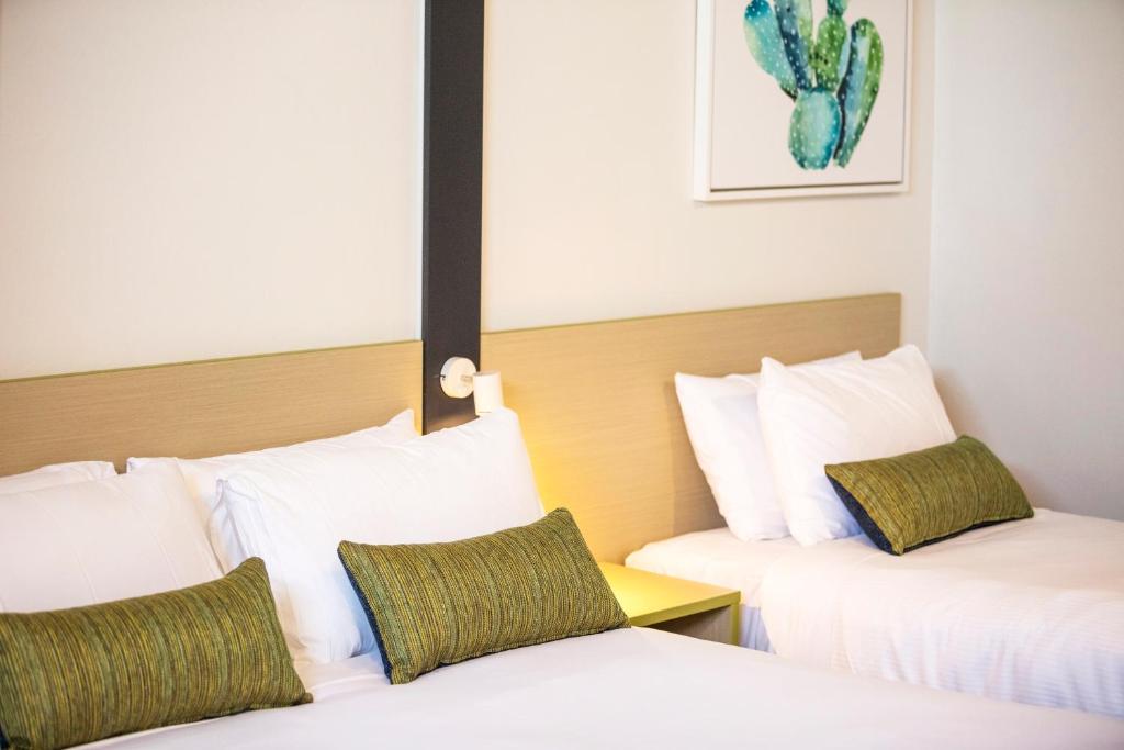 duas camas num quarto de hotel com almofadas brancas e verdes em Nightcap at Hume Hotel em Bankstown