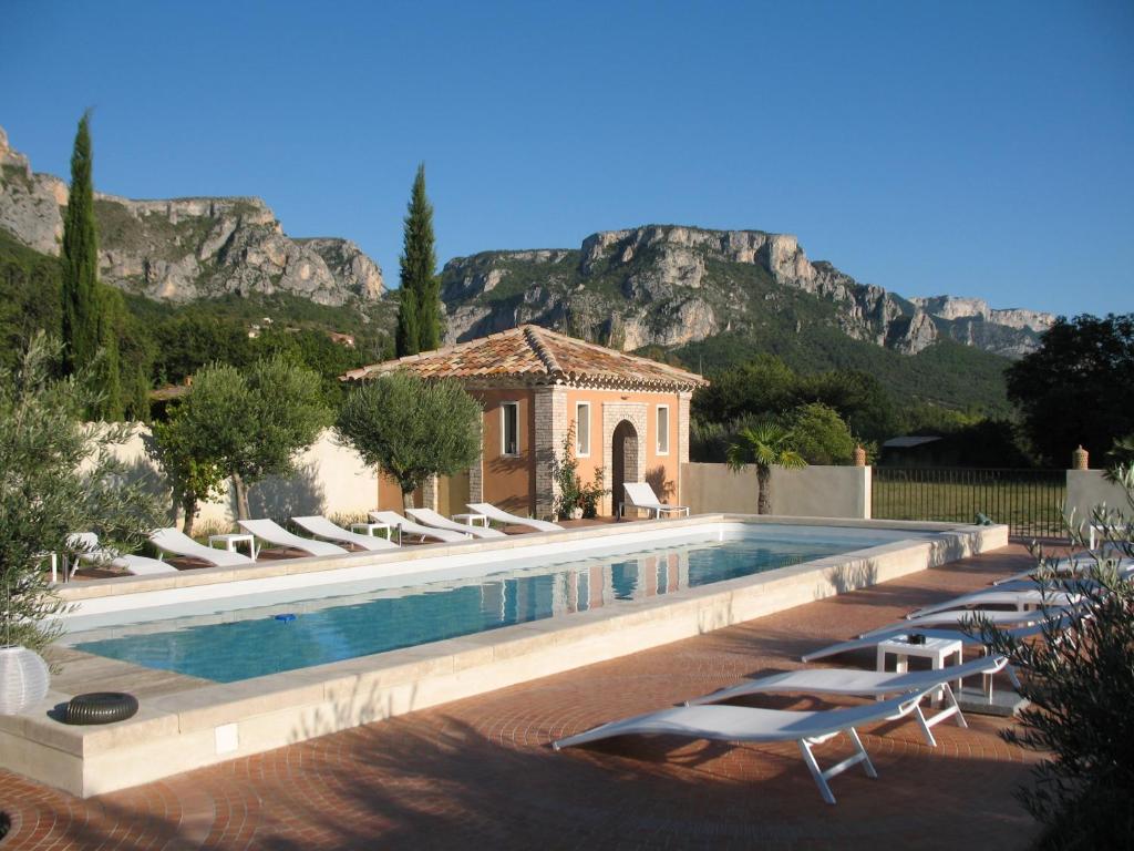a pool with chairs and a house with a mountain in the background at La Ferme Rose-Hôtel de Charme in Moustiers-Sainte-Marie