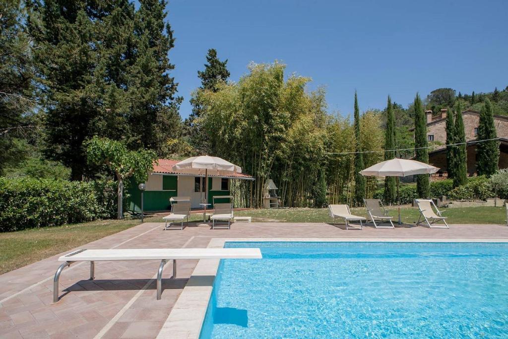 a pool with chairs and umbrellas next to a house at Azienda Agricola e Agriturismo Vallorsi in Terricciola