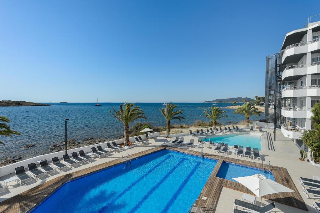 einen Pool mit Stühlen und das Meer in der Unterkunft Apartamentos Vibra Jabeque Dreams in Ibiza-Stadt