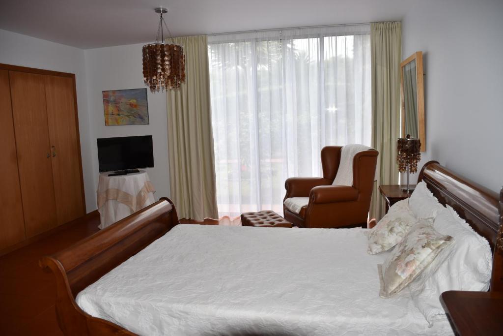 a bedroom with a bed and a chair and a window at Caloura Camellia House in Caloura