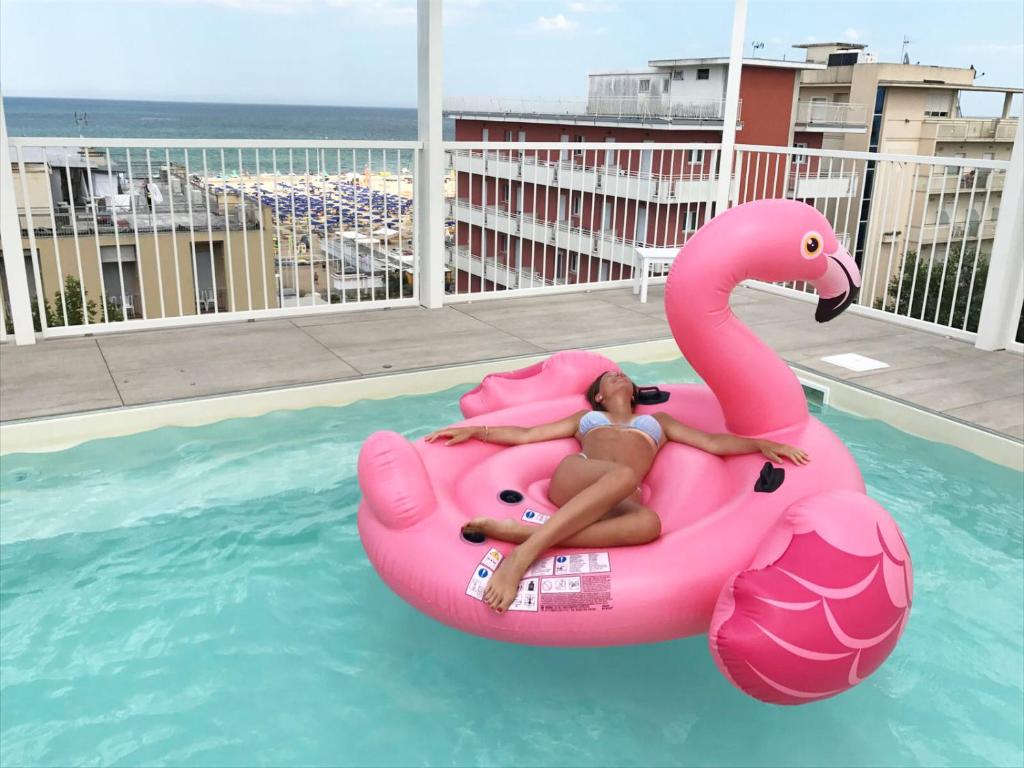 a woman is laying on anlatable pink flamingo in a pool at Residence Ten Suite in Rimini