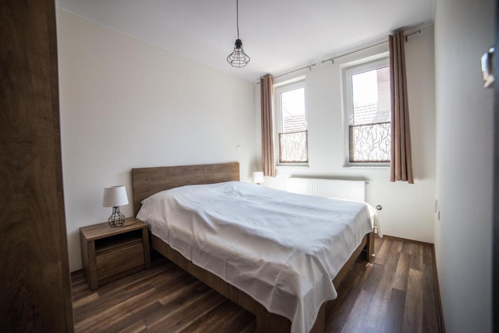 a white bedroom with a bed and two windows at Boka Apartmanház in Gyula