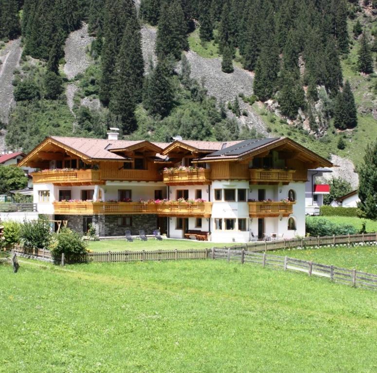a large house in a field next to a mountain at Landhaus Alpensonne in Neustift im Stubaital