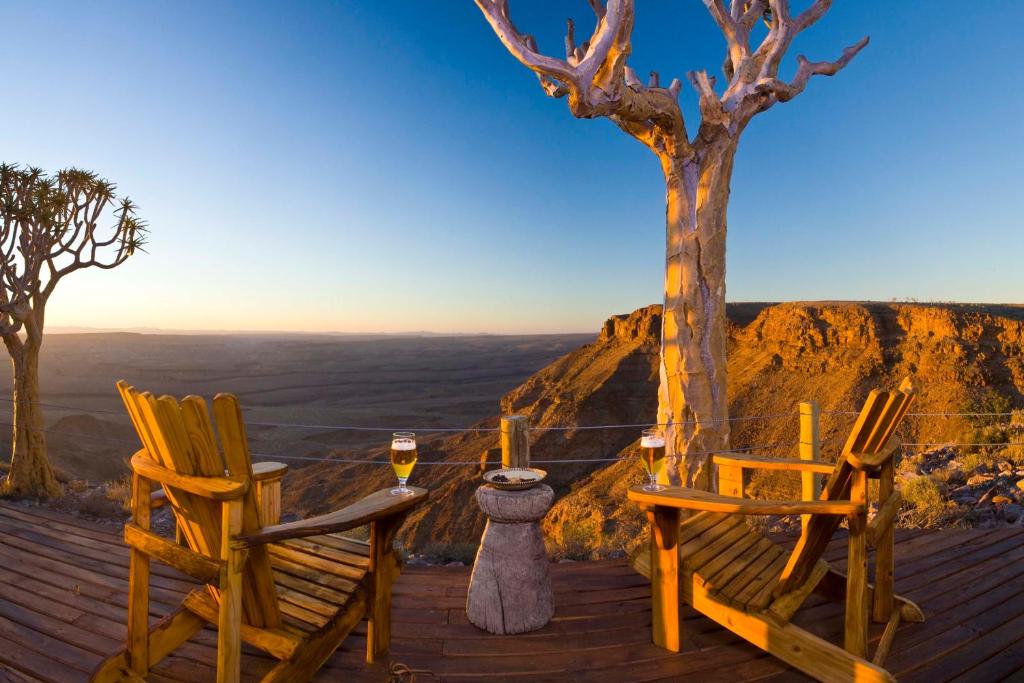 two chairs and a table on a deck with a tree at Fish River Lodge in Ariamab