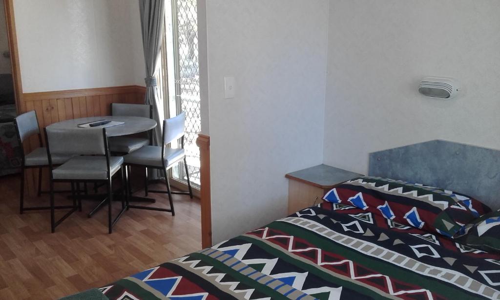 1 dormitorio con 1 cama y 1 mesa con sillas en Acclaim Gateway Tourist Park, en Norseman