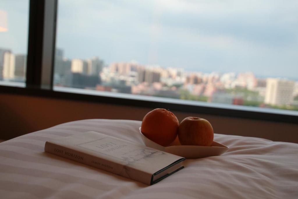 a book and two oranges on a bed with a window at Shangri-La Far Eastern Tainan in Tainan