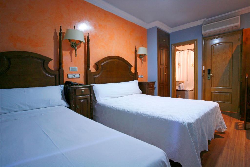2 camas num quarto com paredes cor-de-laranja em Hostal Victoria II em Madrid