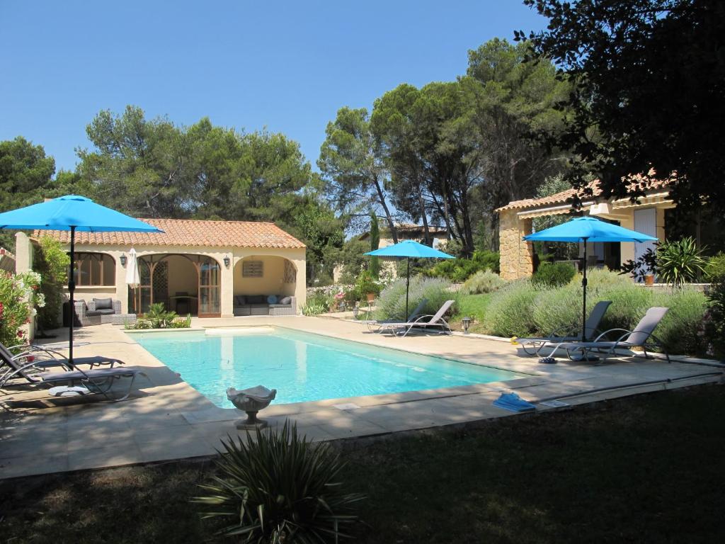 a swimming pool with two blue umbrellas and chairs at L&#39;Oustau de Bigatié in Lambesc