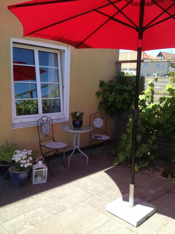 a red umbrella on a patio with a table and chairs at Sommerlyst in Løkken