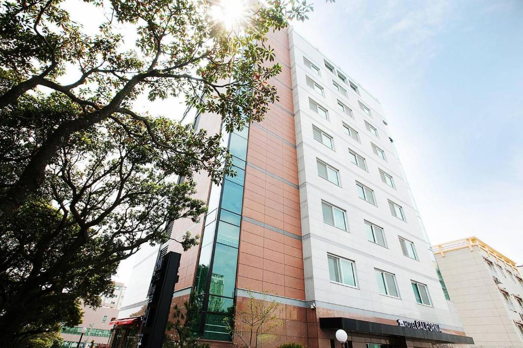 a tall white and red building with trees in front of it at Hotel California in Seogwipo