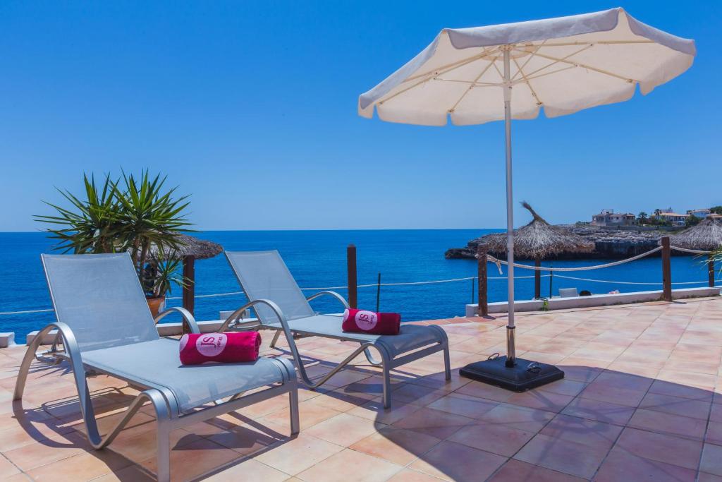 two chairs and an umbrella on a patio with the ocean at JS Cape Colom - Adults Only in Portocolom