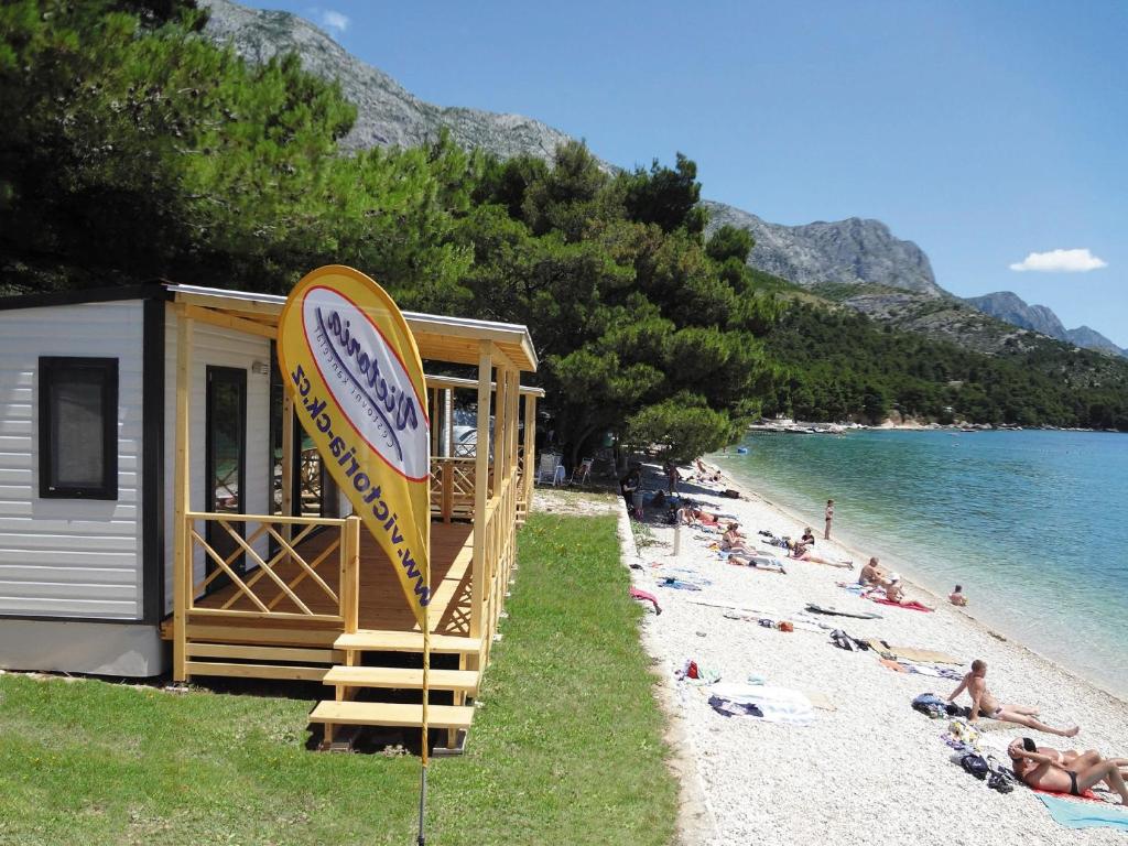 a building on a beach with people laying on the sand at Victoria Mobilhome Camping Dole-Živogošče in Blato