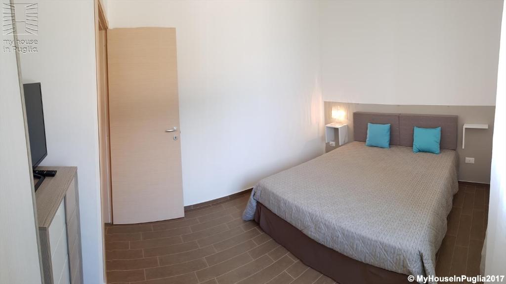 a bedroom with a bed with blue pillows and a television at Case Vacanza Marzano in Monopoli