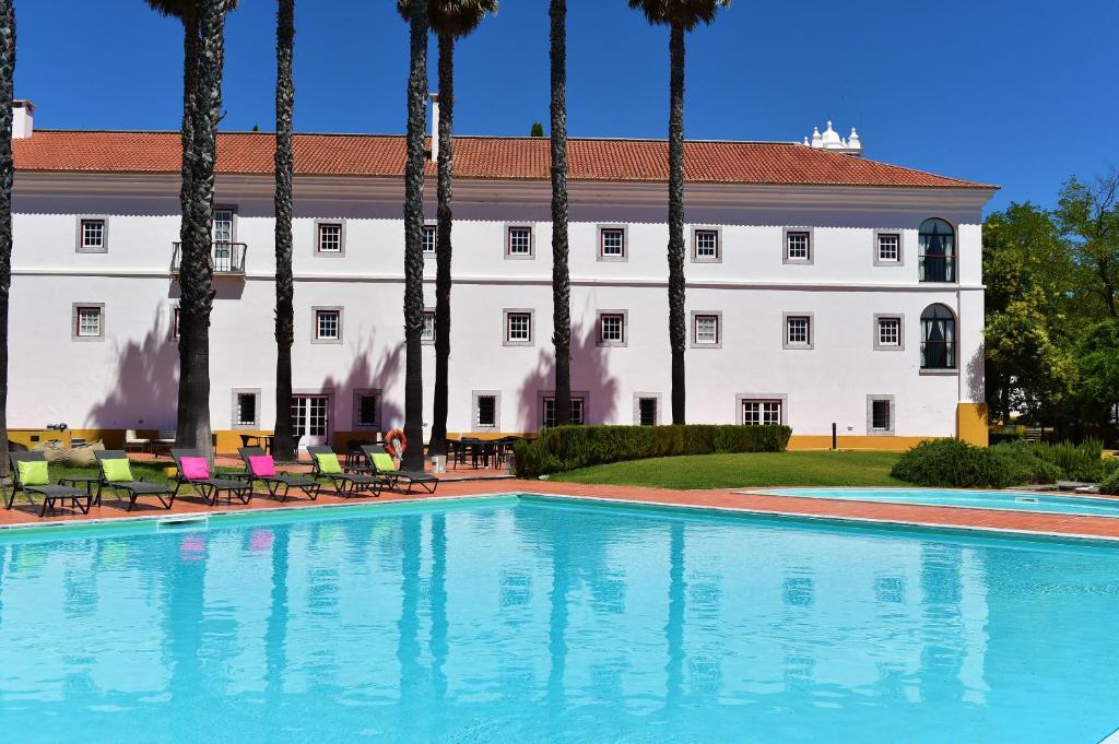 a swimming pool in front of a building with palm trees at Pousada Convento de Beja in Beja