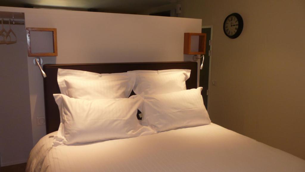 a bed with white pillows and a clock on the wall at Le Porche de Sarlat in Sarlat-la-Canéda