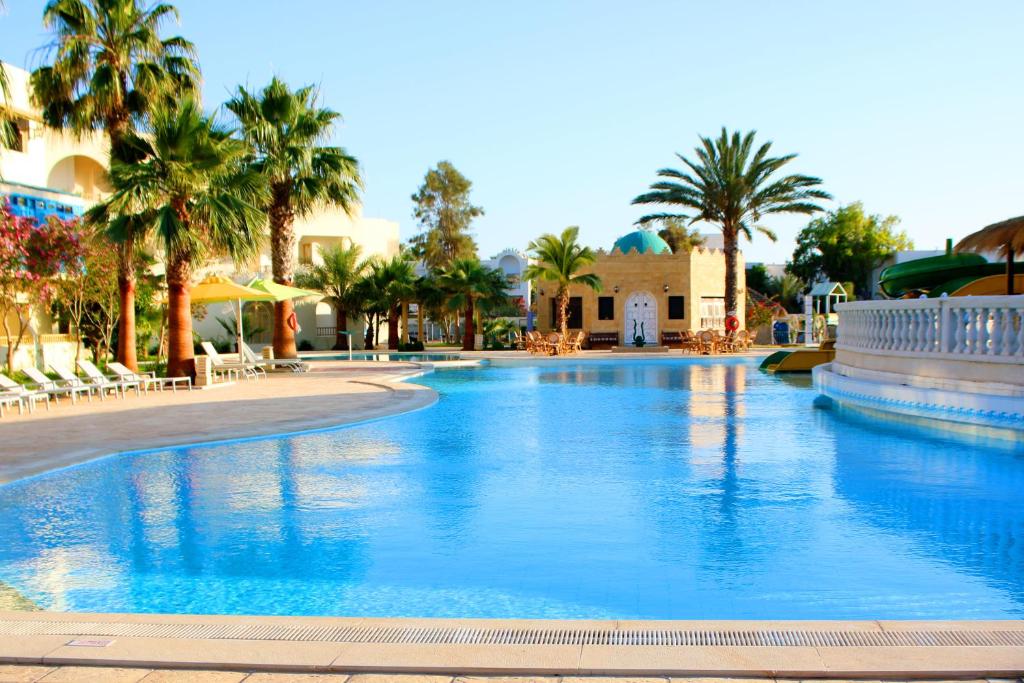 - une grande piscine avec des palmiers dans un complexe dans l'établissement The Ksar Djerba Charming Hotel & SPA, à Midoun