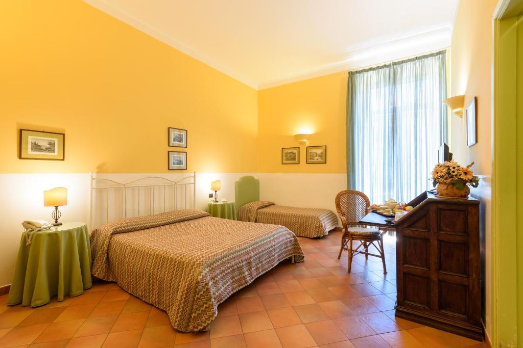 a bedroom with two beds and a desk and a window at Hotel Mergellina in Naples