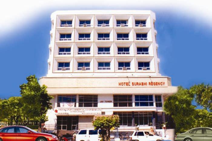 un bâtiment blanc avec des voitures garées devant lui dans l'établissement Hotel Surabhi Regency, à Anand