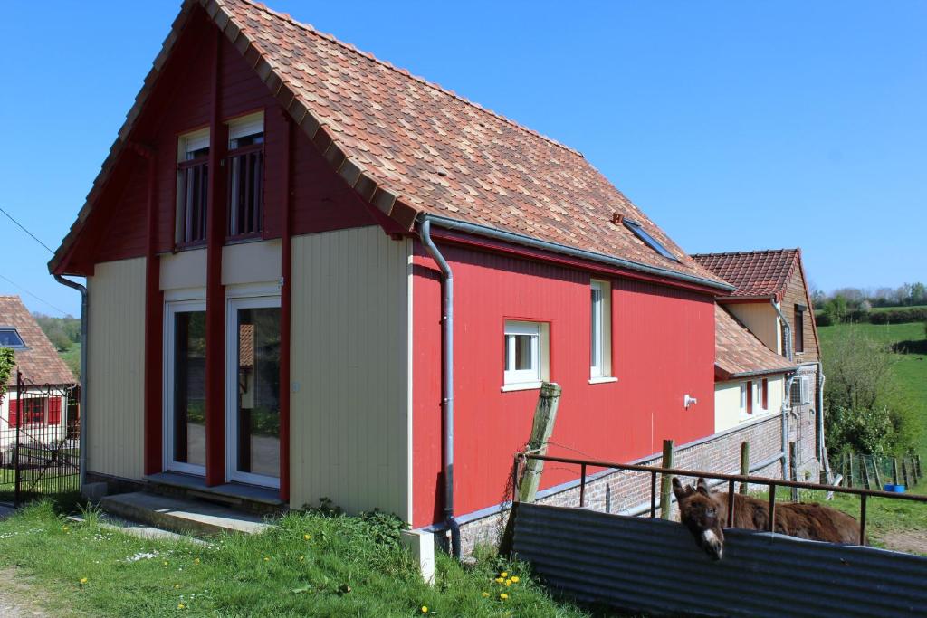 une maison rouge et blanche avec un chien debout à côté dans l'établissement La Grange Du Festel, à Oneux