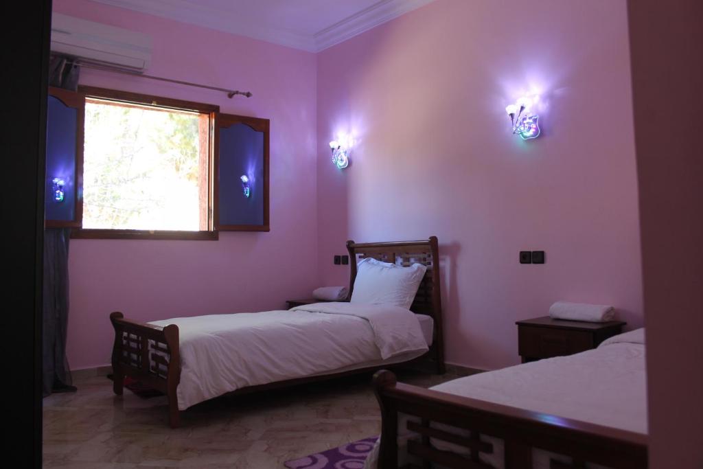 two beds in a room with pink walls and a window at Hôtel Ajil Cascades D'ouzoud in Ouzoud