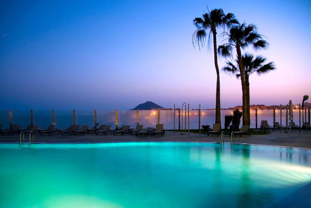 a swimming pool with palm trees and the ocean at dusk at Kn Hotel Arenas del Mar Adults Only in El Médano