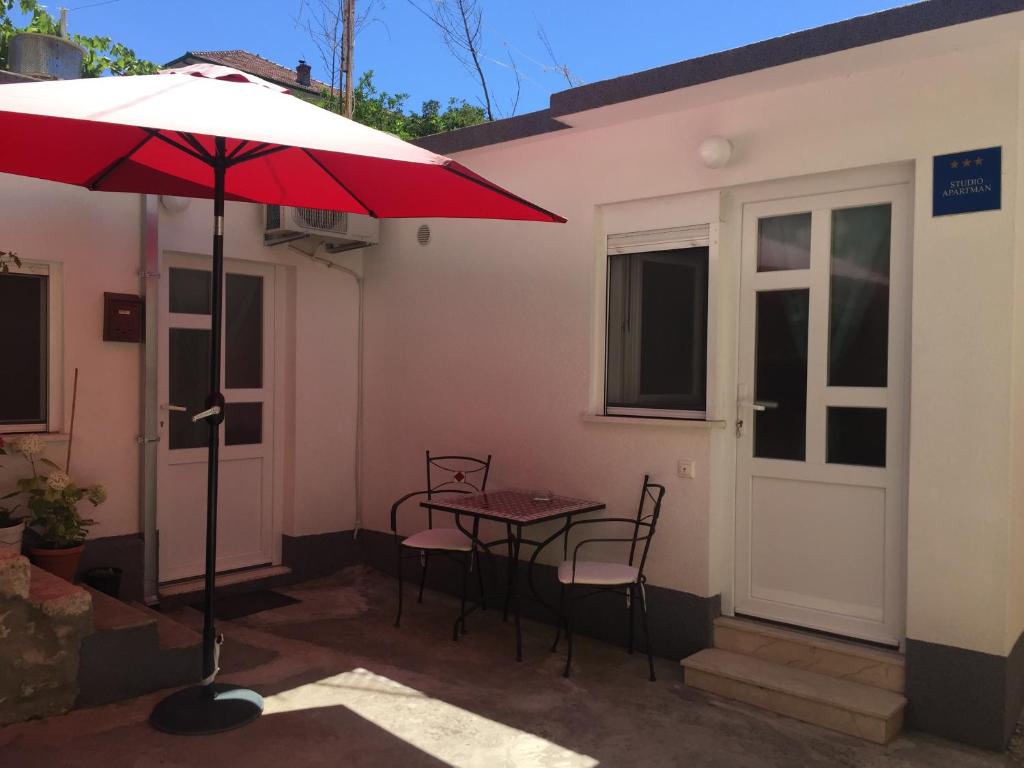 eine Terrasse mit einem Tisch, Stühlen und einem roten Regenschirm in der Unterkunft Dinka Apartment in Trogir