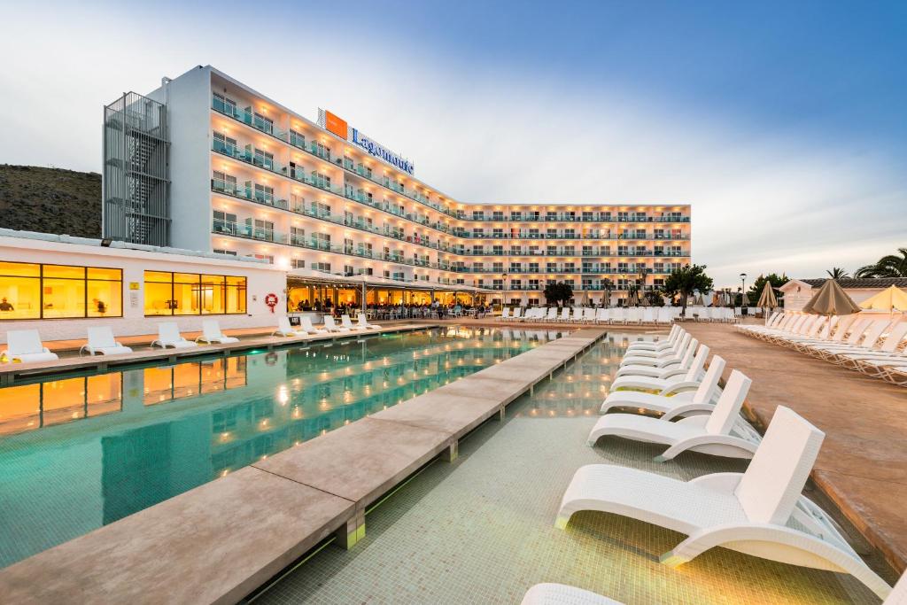 une piscine avec des chaises blanches et un bâtiment dans l'établissement Bellevue Lagomonte, à Port d'Alcúdia