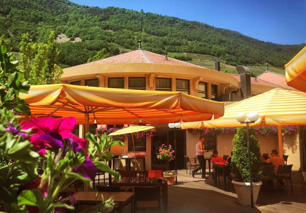 ein Gebäude mit Tischen und Sonnenschirmen davor in der Unterkunft Hotel Restaurant La Porte d'Octodure in Martigny-Ville