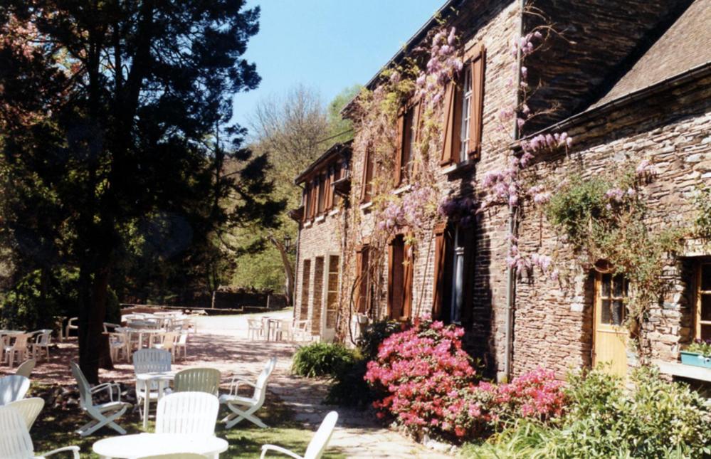 - un bâtiment en pierre avec des chaises, des tables et des fleurs blanches dans l'établissement Auberge Au Naturel des Ardennes, à Rochehaut