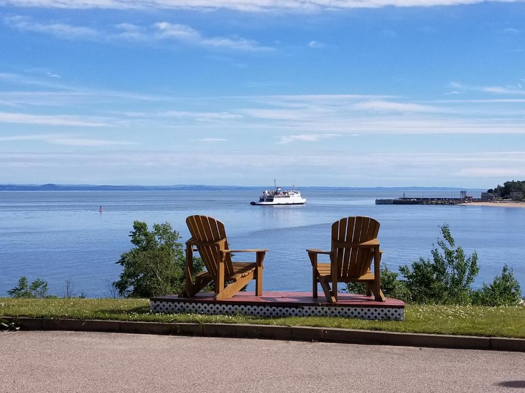 two chairs sitting on a table on the water with a boat at Motel et Chalets Bo-Fleuve Evangeline in Saint-Siméon