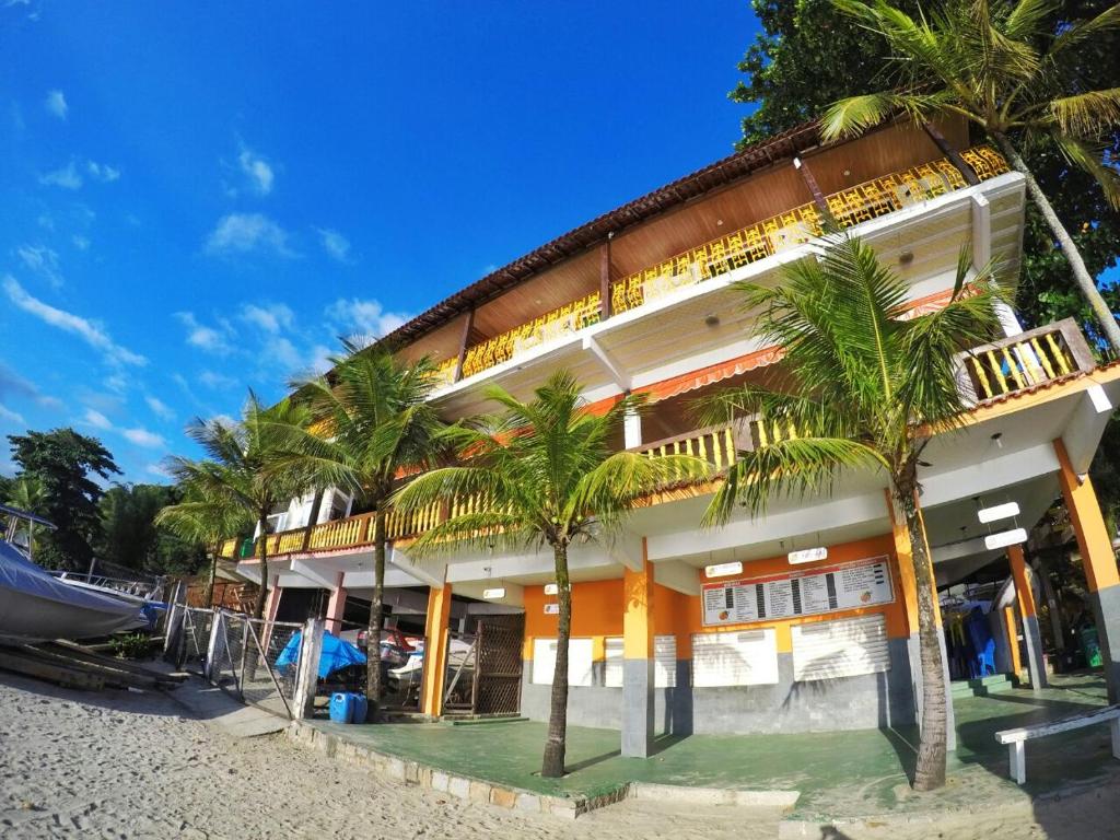 a building on the beach with palm trees in front at Pousada da Praia in Mangaratiba