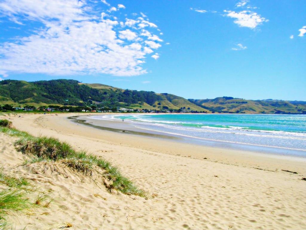 una playa de arena con el océano y las montañas en el fondo en Rayville Boat Houses, en Apollo Bay