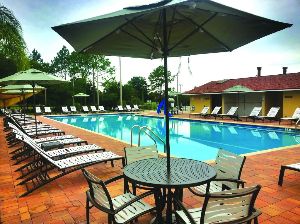 a table and chairs with an umbrella next to a swimming pool at Orlando RV Resort in Orlando