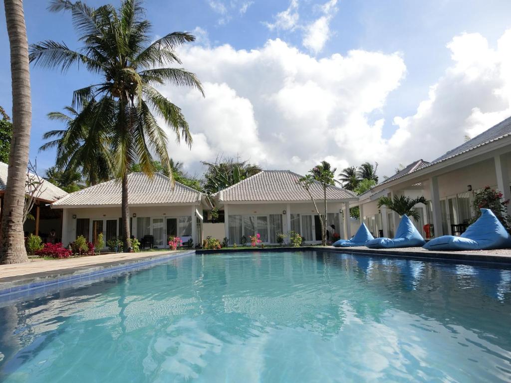 a swimming pool in front of a house with palm trees at Lombok Holiday Hotel in Kuta Lombok