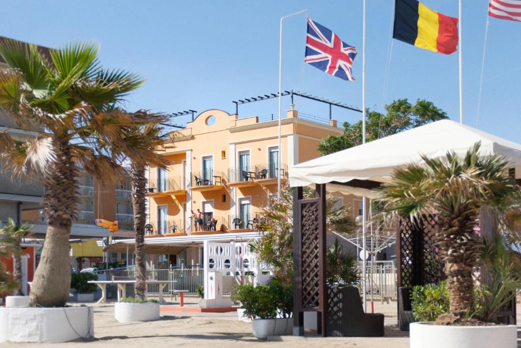 two flags flying in front of a building with palm trees at Hotel Holiday Beach in Rimini