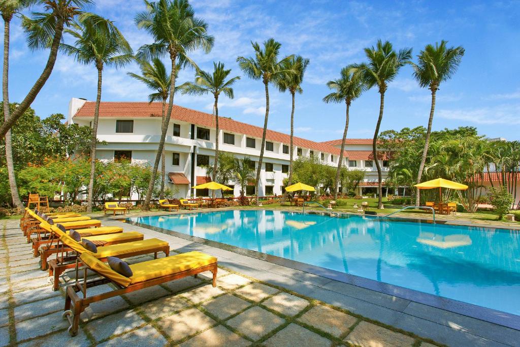 a resort pool with lounge chairs and palm trees at Trident Chennai in Chennai