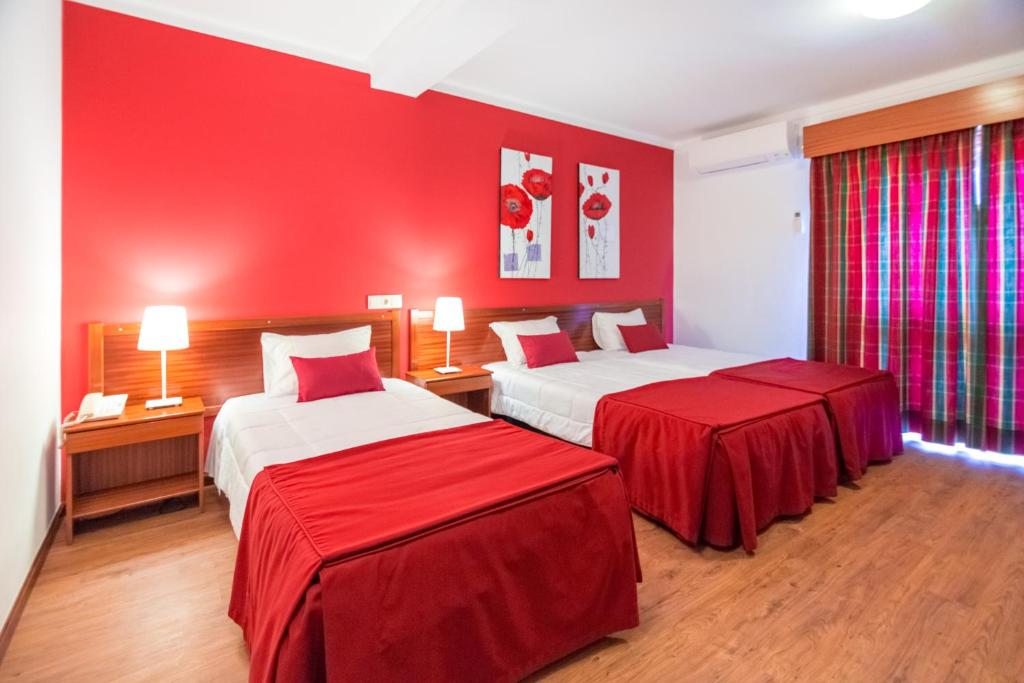 a hotel room with two beds with red walls at Hotel Cristo Rei - Fatima in Fátima