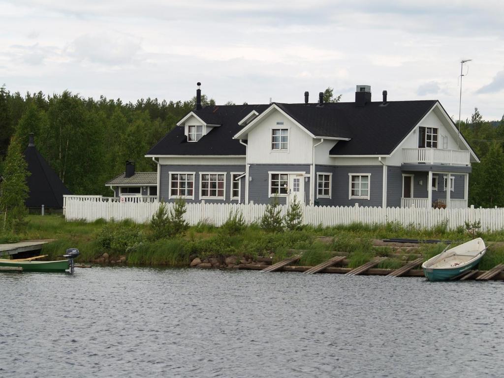 a white house with a white fence and a boat on the water at Miekojärvi Resort in Sirkkakoski